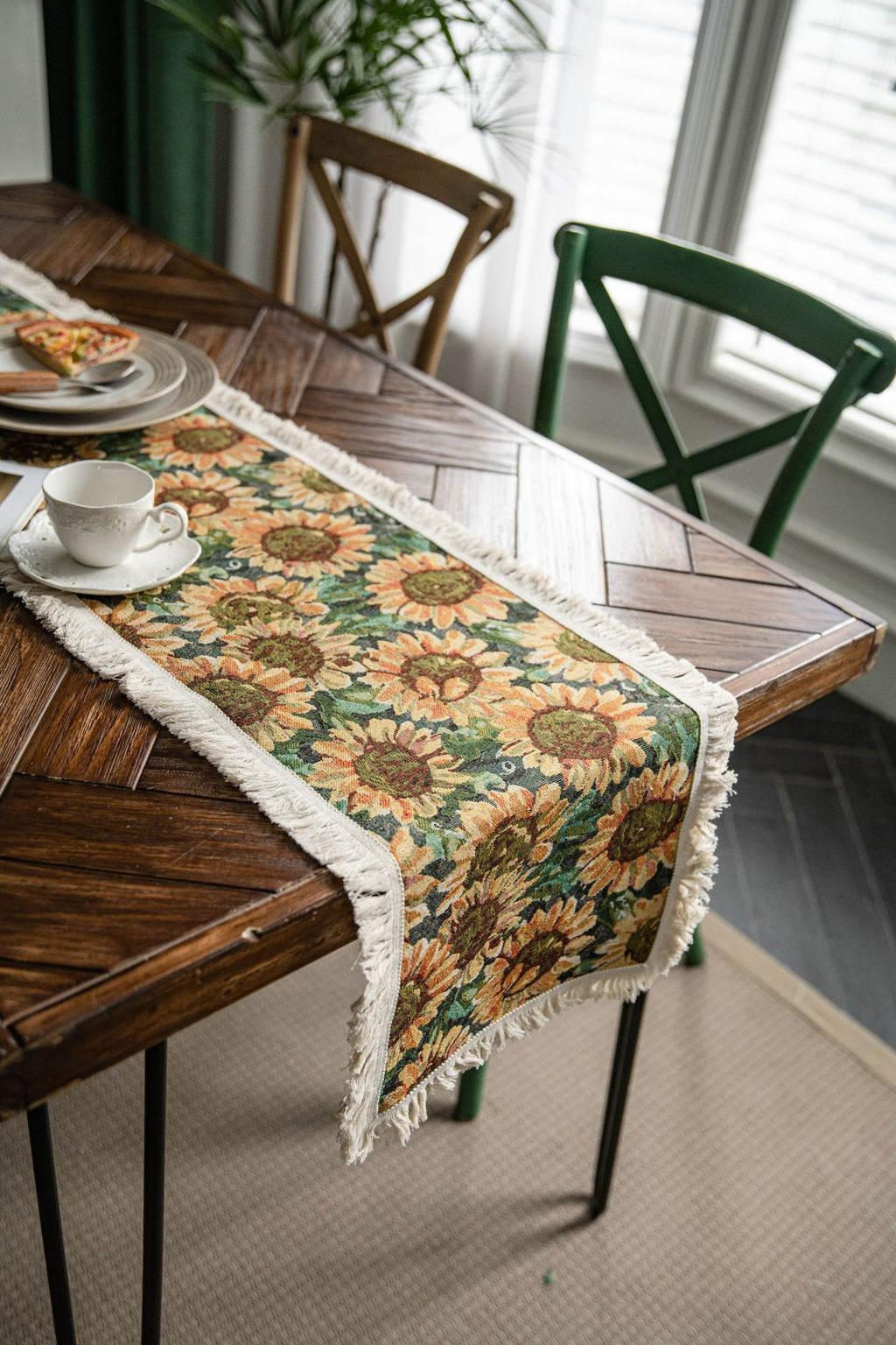 Table with a sunflower patterned table runner and green chairs in a room.