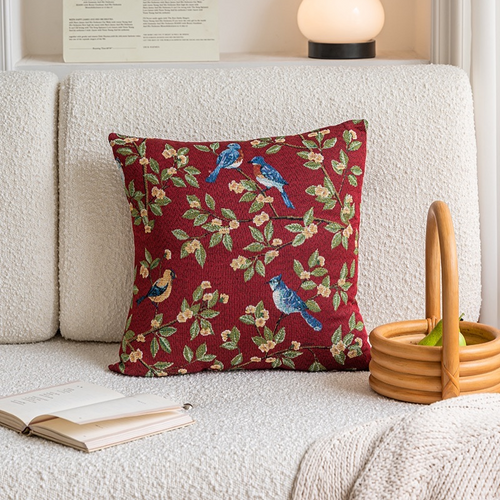 Decorative pillow with bird pattern on a white sofa with a lamp and basket in the background.