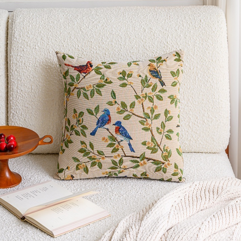 Decorative pillow with bird design on a white sofa with a book and small table.