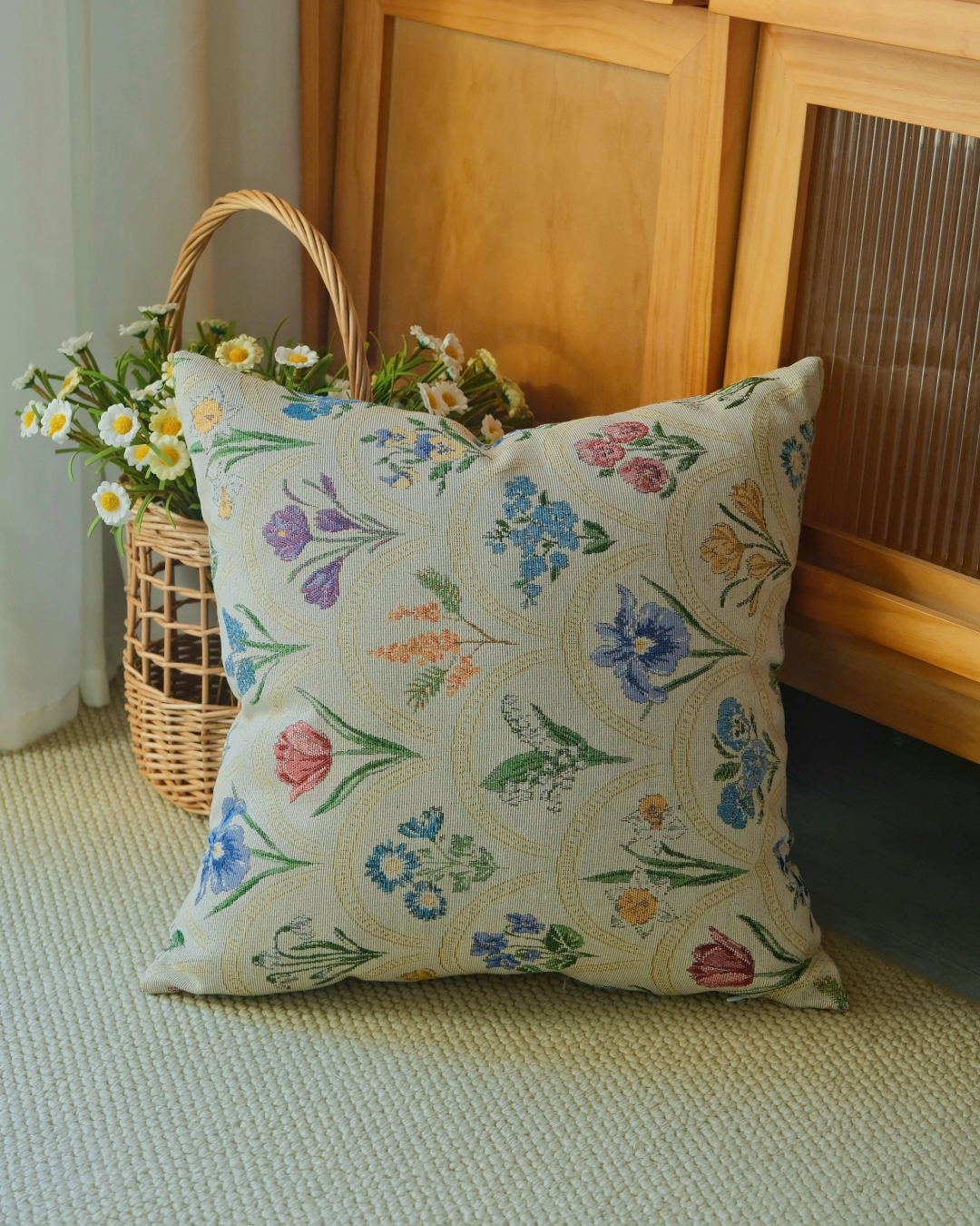 Watercolor floral pillow cover styled on a rug beside a wicker flower basket