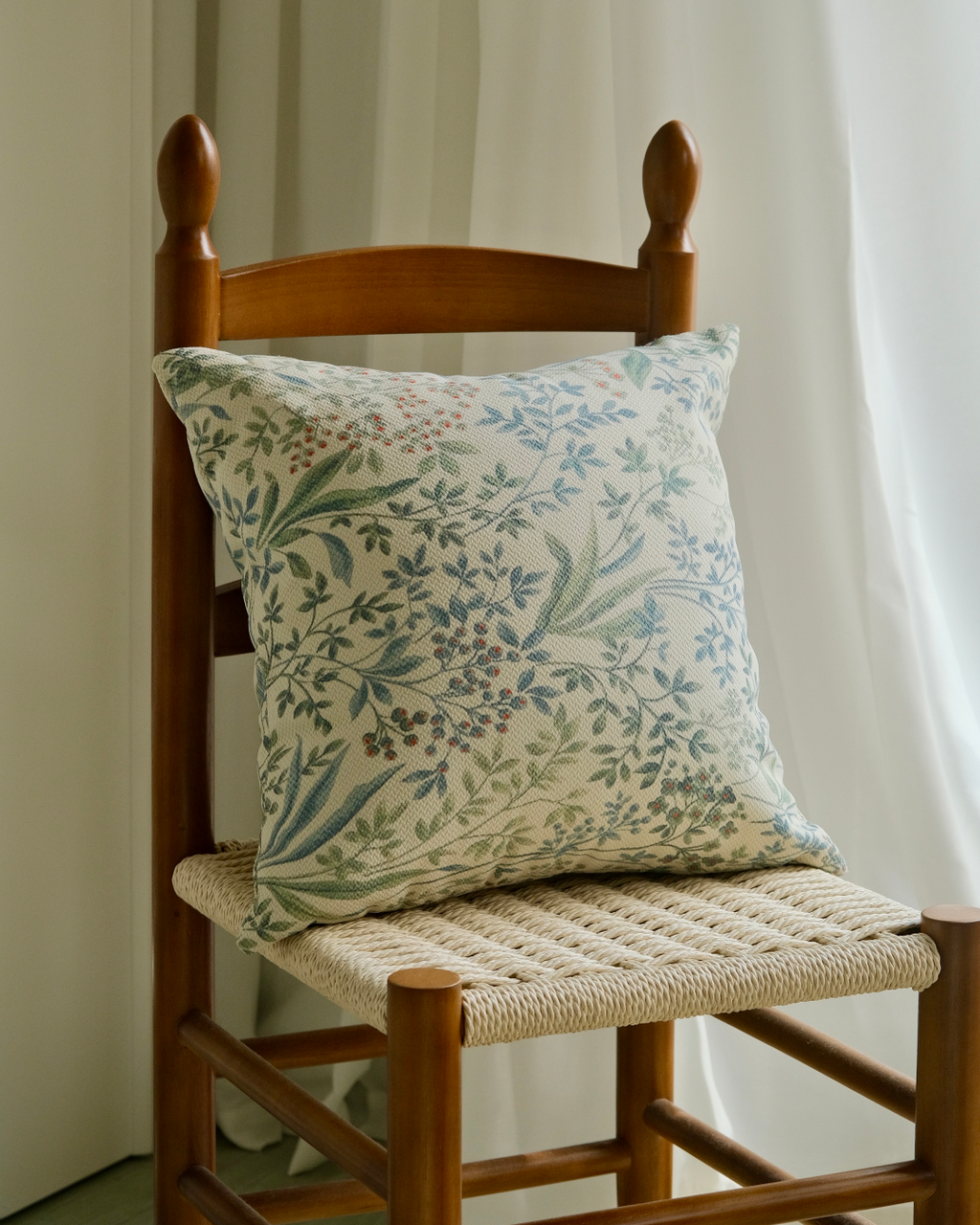 Sage green sprig cushion cover on a chair against white curtains