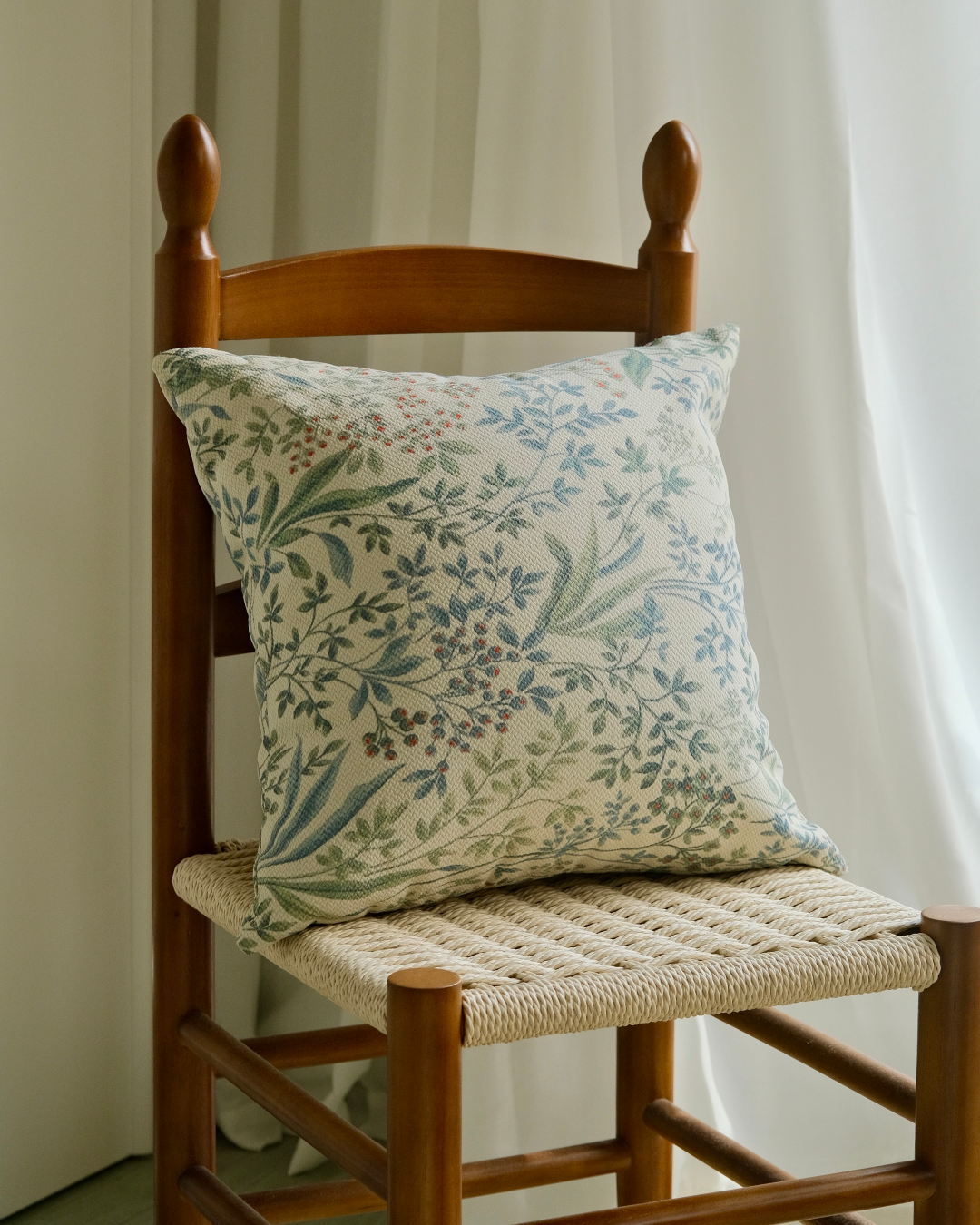 Sage green sprig cushion cover on a chair against white curtains