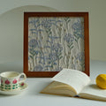 Walnut-finish framed fabric decor beside a floral teacup and book on a round table