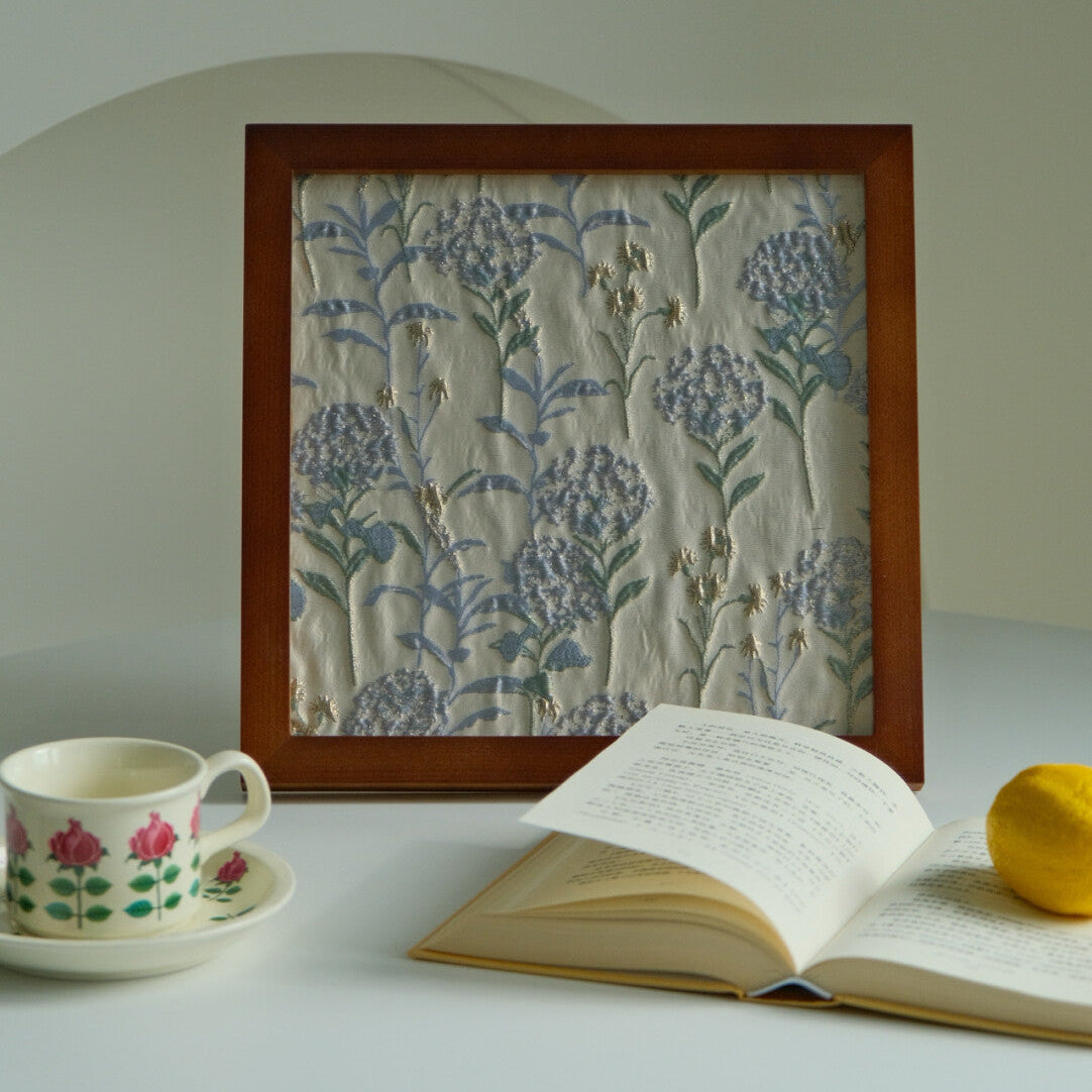 Walnut-finish framed fabric decor beside a floral teacup and book on a round table