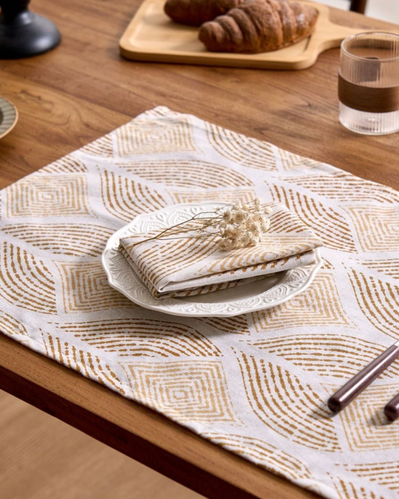 Table setting with a patterned placemat, folded napkin, and cutlery on a wooden table.