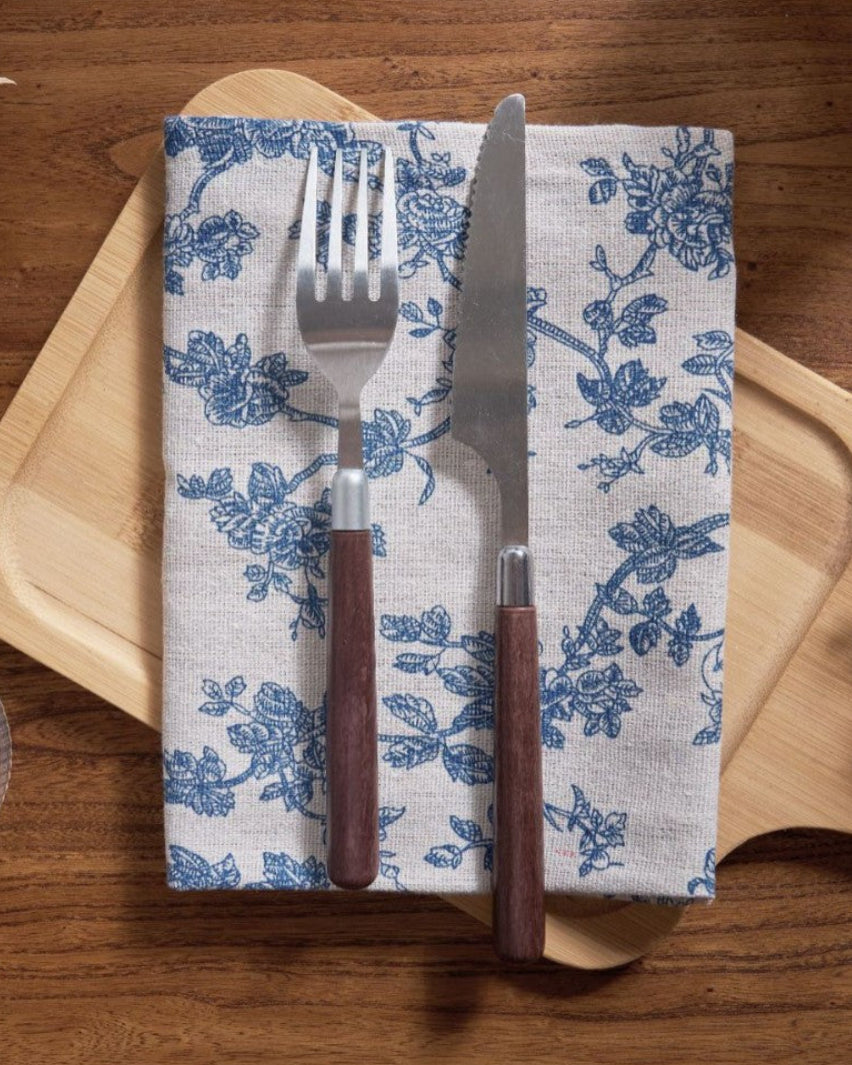 Blue floral napkin folded with cutlery on a wood board