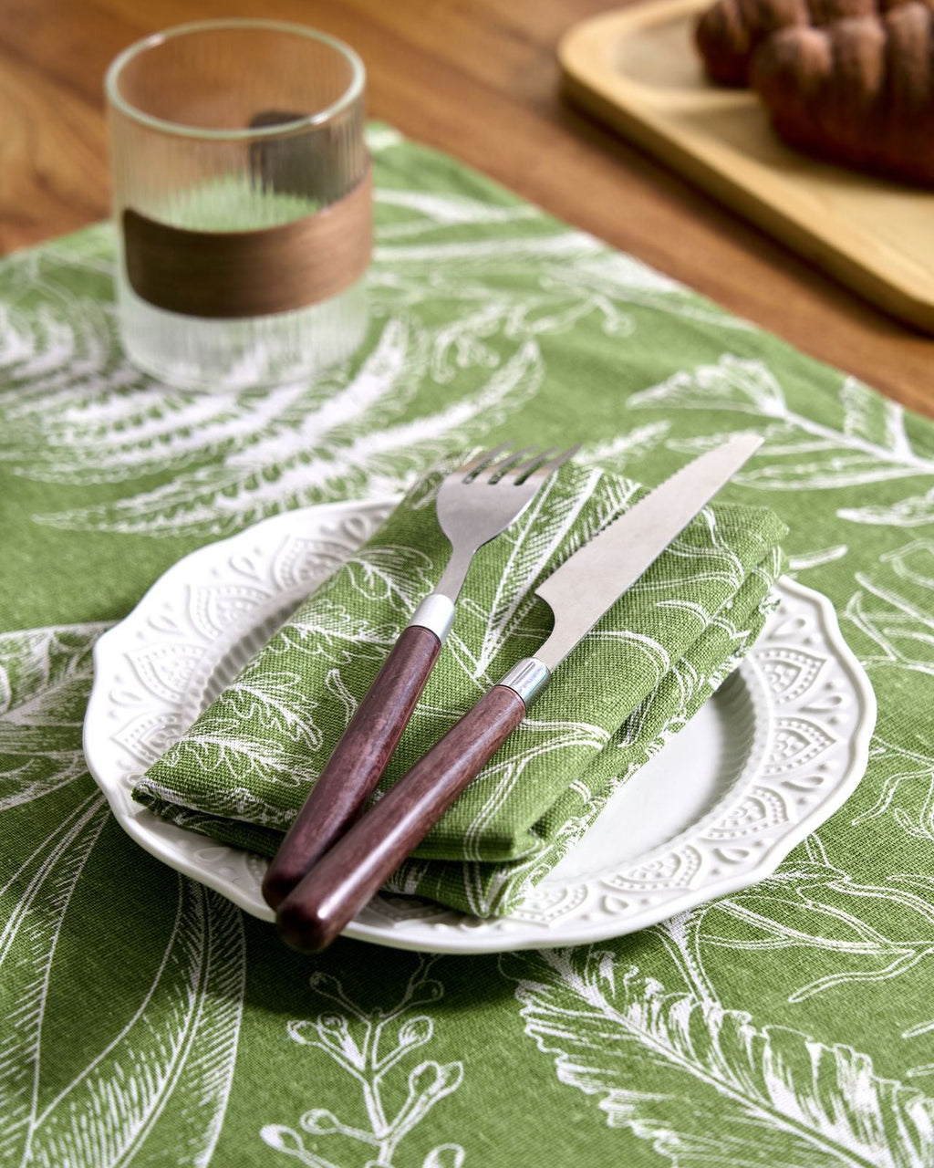Sage green fern napkin folded with cutlery on a plate