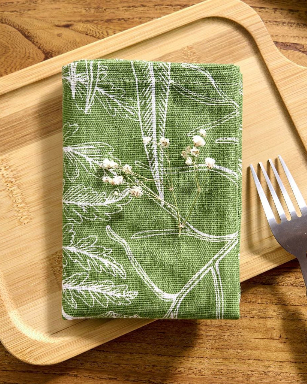 Folded sage green botanical napkin on a wood board