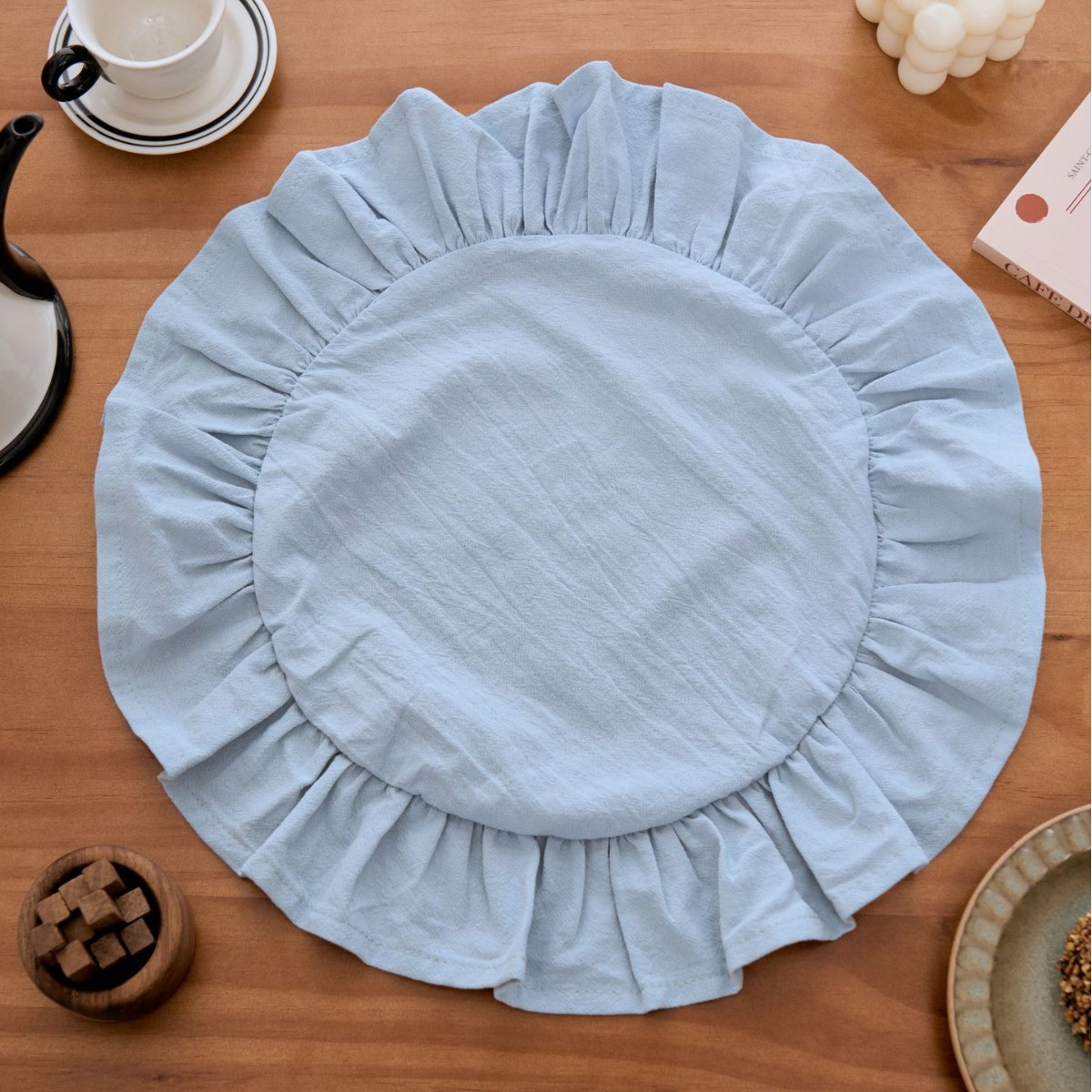 Light blue round placemat on a wooden table with a cup and saucer in the background.