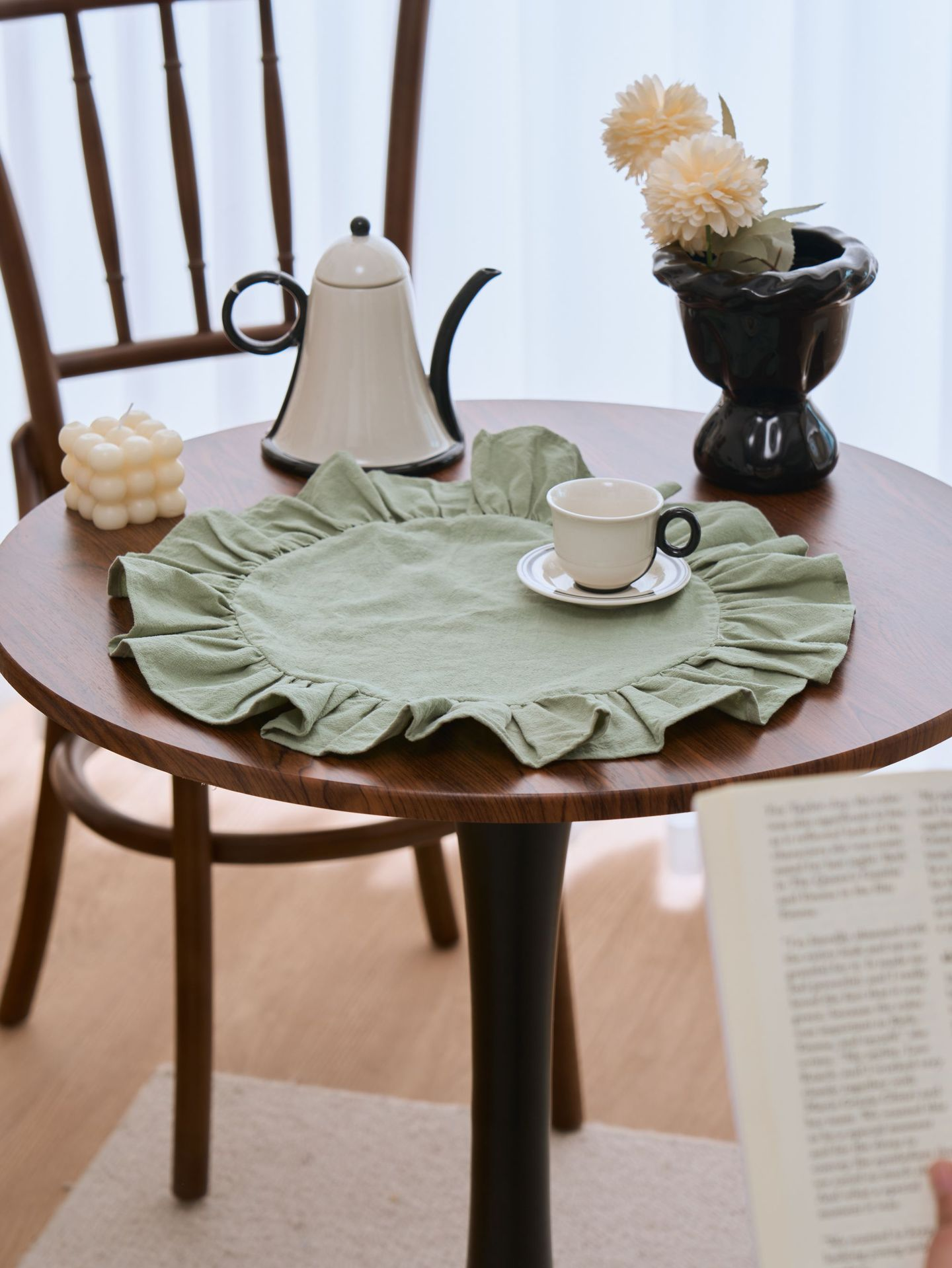 Round wooden table with a green placemat, teacup, and teapot in a cozy room.