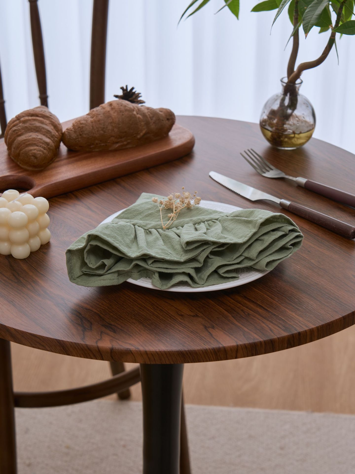 Green folded napkin on a wooden table with croissants, a cutting board, and a plant in the background.