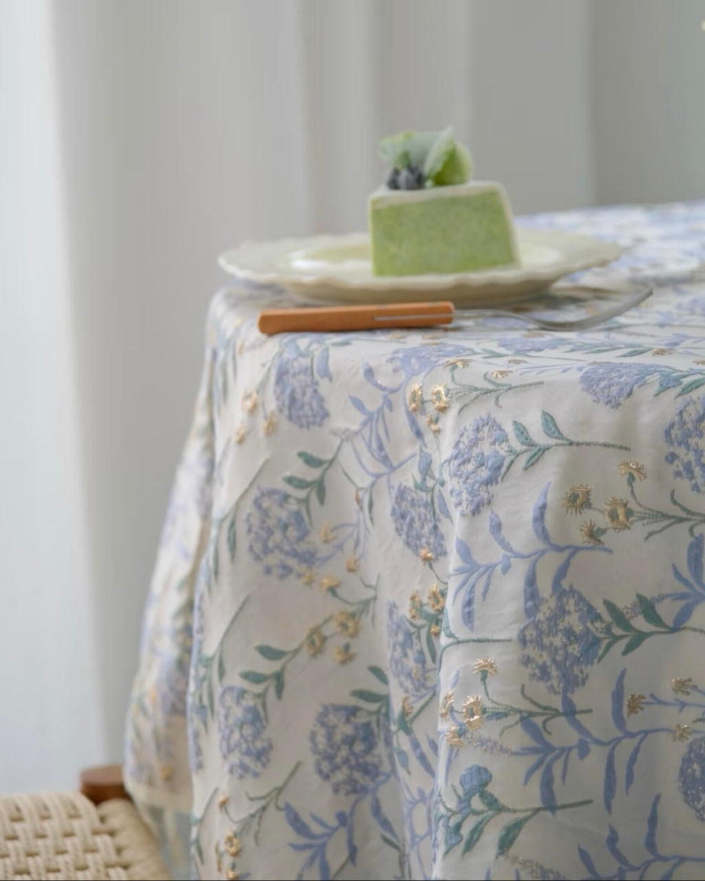 Table with floral tablecloth and a small cake on a white plate.
