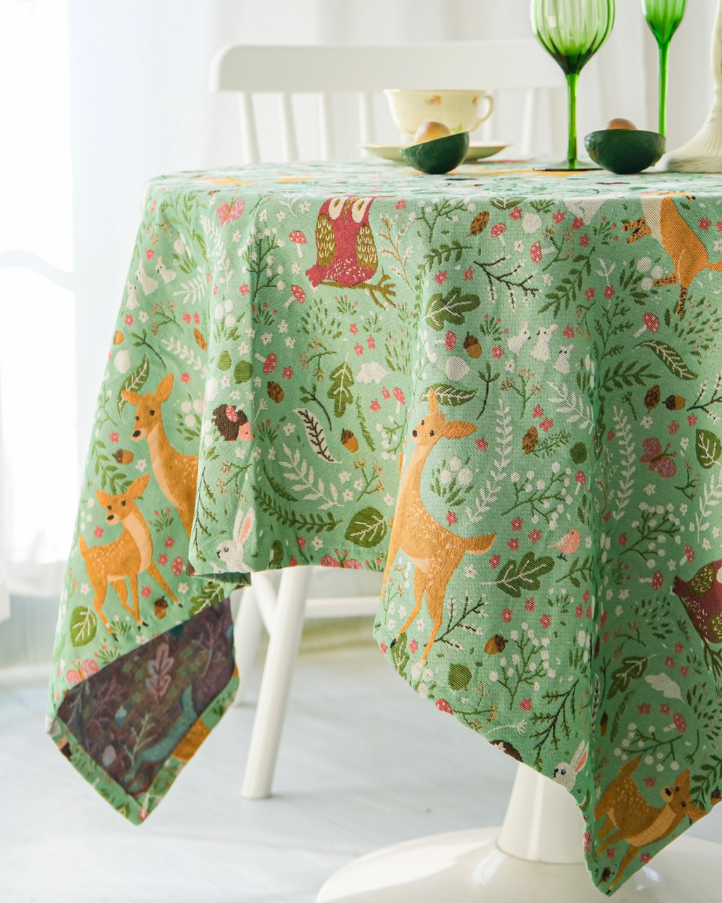 Woodland tablecloth draped over table edge with green glassware