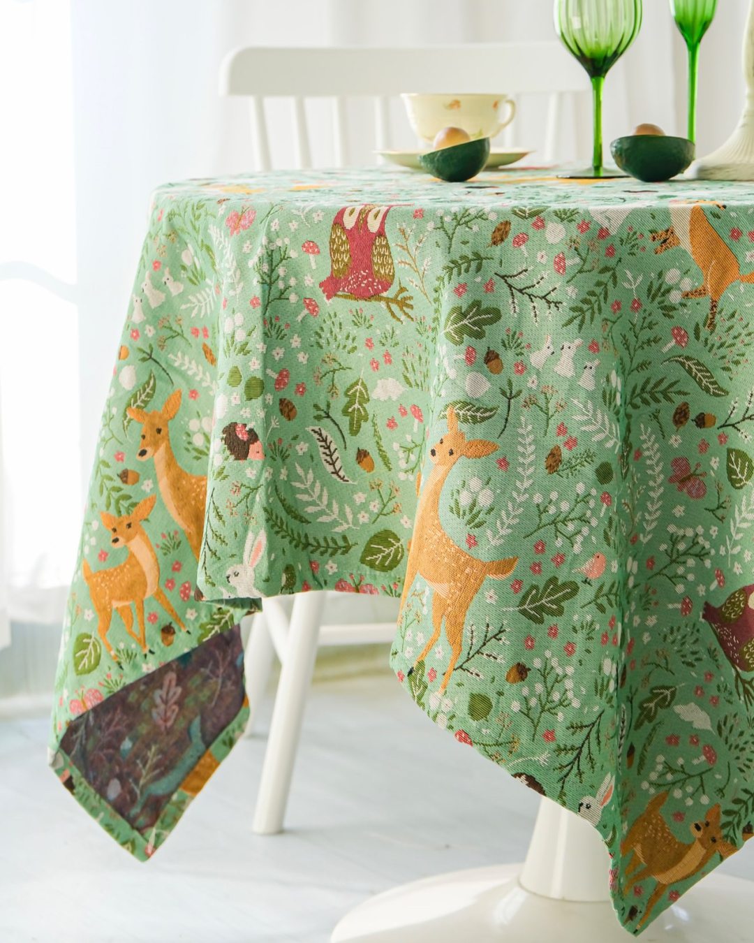 Woodland tablecloth draped over table edge with green glassware
