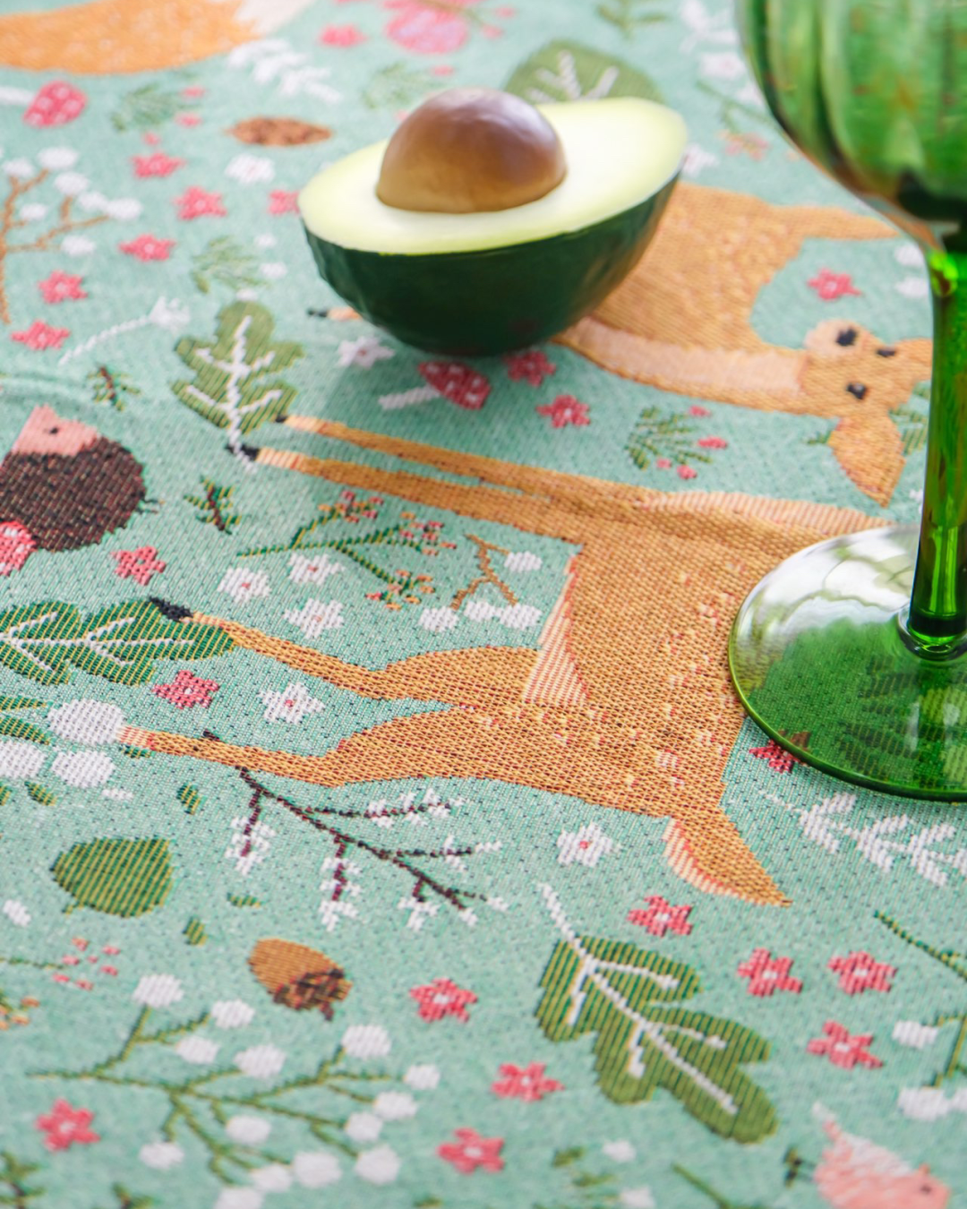 Close view of fox print on woodland tablecloth with avocado and green glass