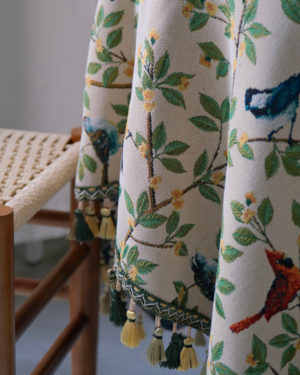 Tassel trim detail on Bluebird Garden tablecloth beside a wooden chair