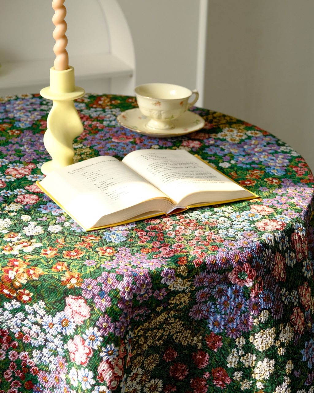 Dark floral tablecloth on a round table with candlesticks and a teacup