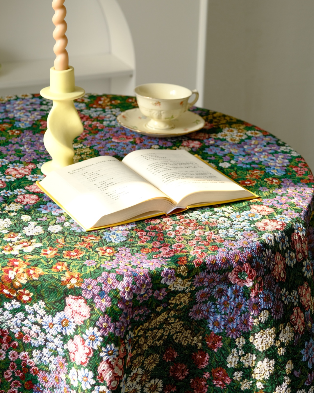 Dark floral tablecloth on a round table with candlesticks and a teacup
