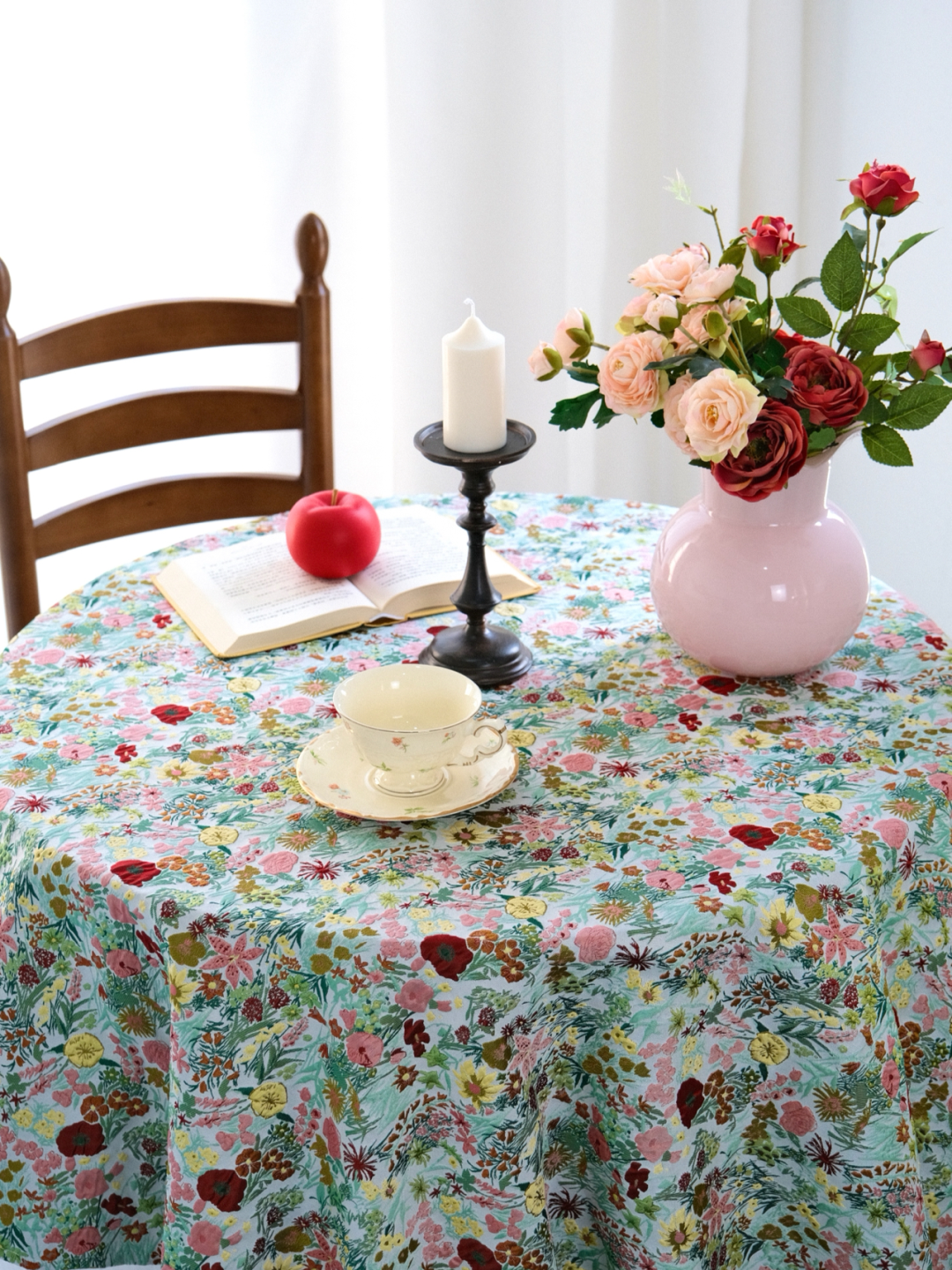 Bright floral tablecloth on a table with pink vase and candlestick