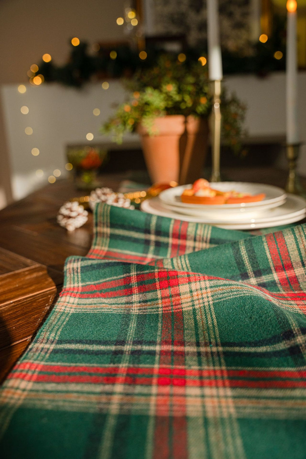 Table setting with a plaid tablecloth, plates, and a candle in a cozy indoor setting.