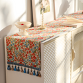 Red floral tasseled table runner on a console table with a vase and picture frame
