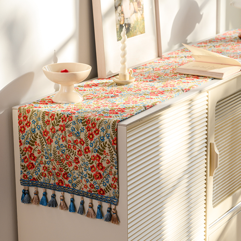 Red floral tasseled table runner on a console table with a vase and picture frame