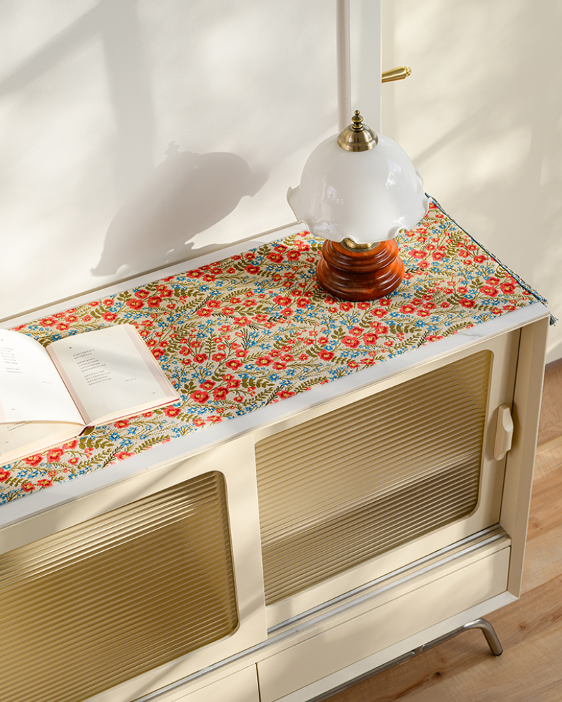 Red floral table runner on a console table with a lamp and books