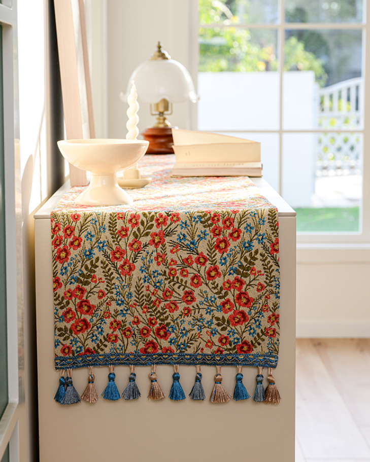 Red floral tasseled table runner on a console table by a bright window