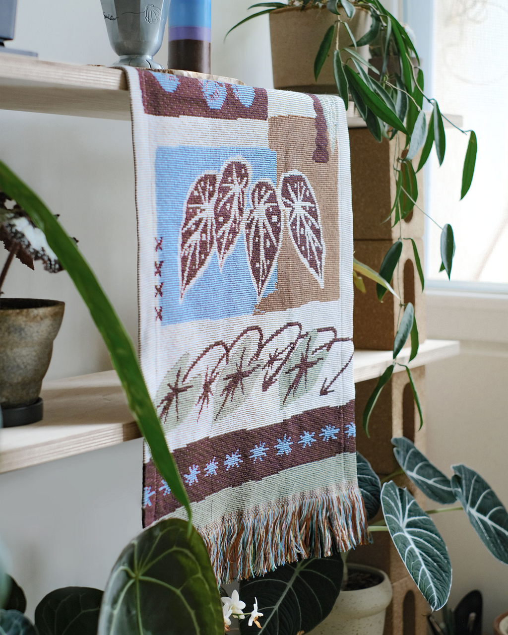 Close view of woven leaf pattern tapestry with fringe among monstera leaves