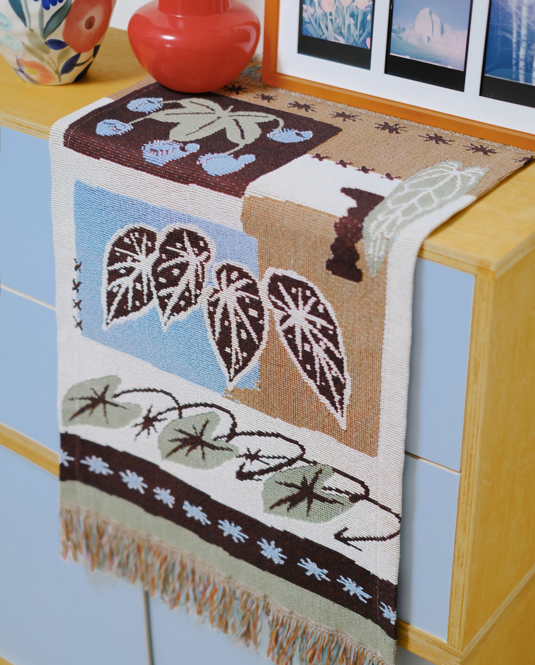 Woven fringe runner styled on a dresser corner with a red vase